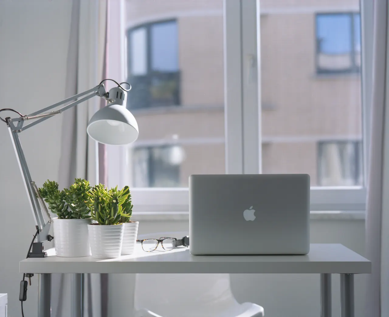 A bright, quiet workspace with a laptop, a desk lamp and a plant