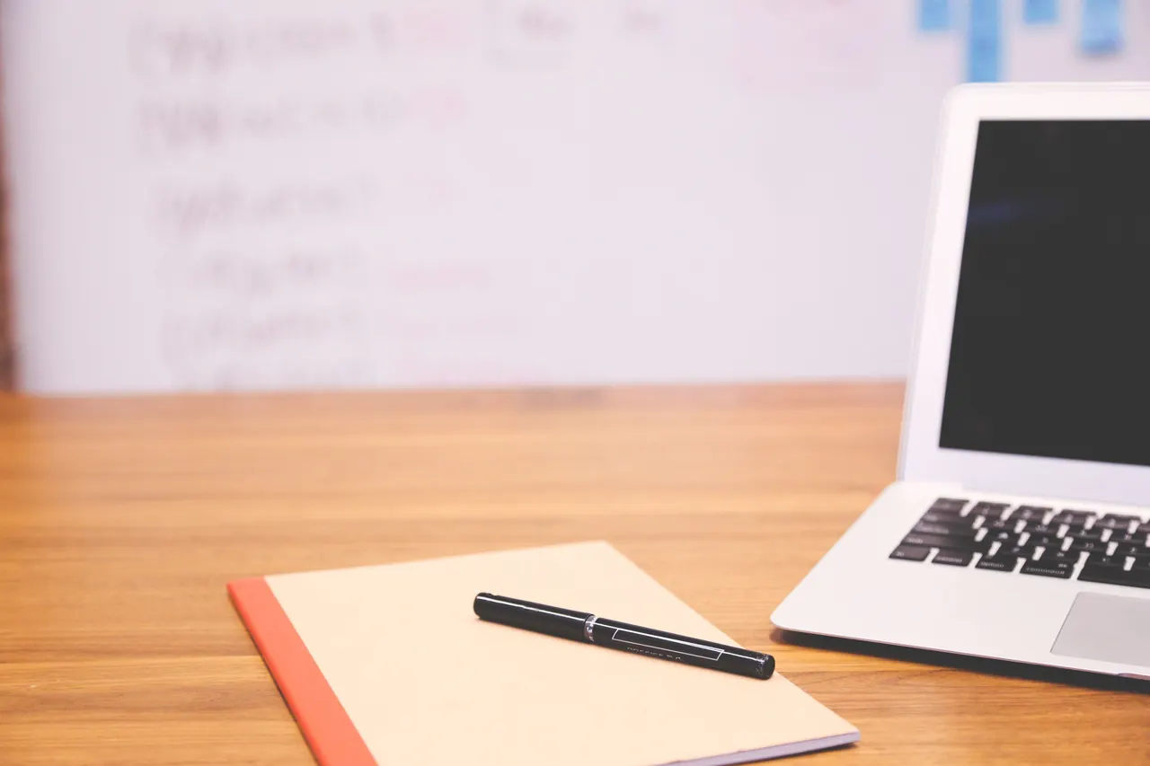 A modern desk with a laptop, a notebook and a pen