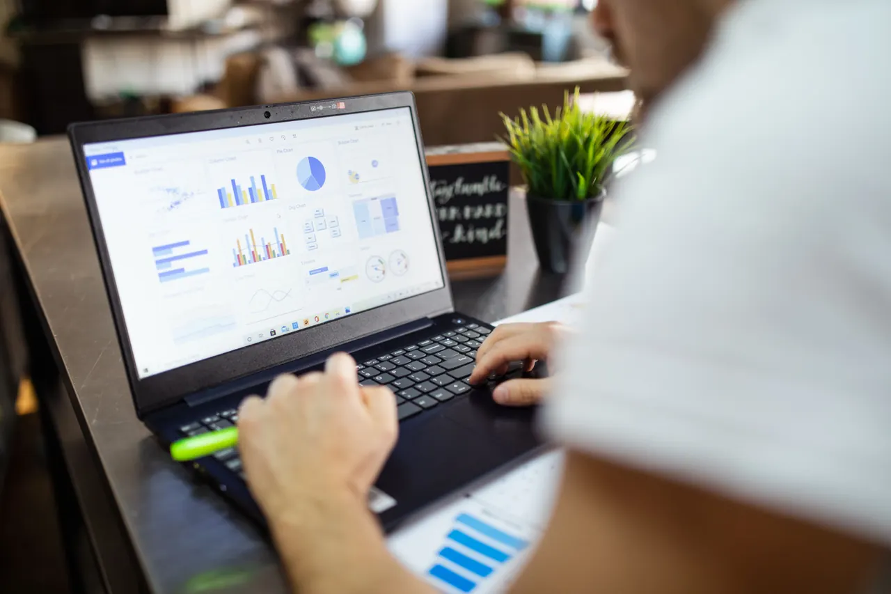 A laptop showing charts and a spreadsheet being reviewed at a desk