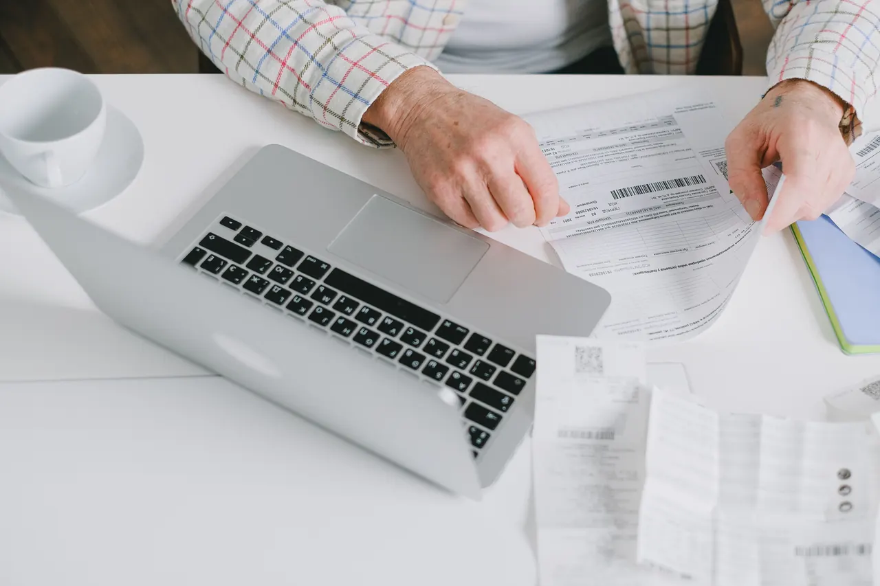 Hands sorting receipts and documents on a desk next to a laptop